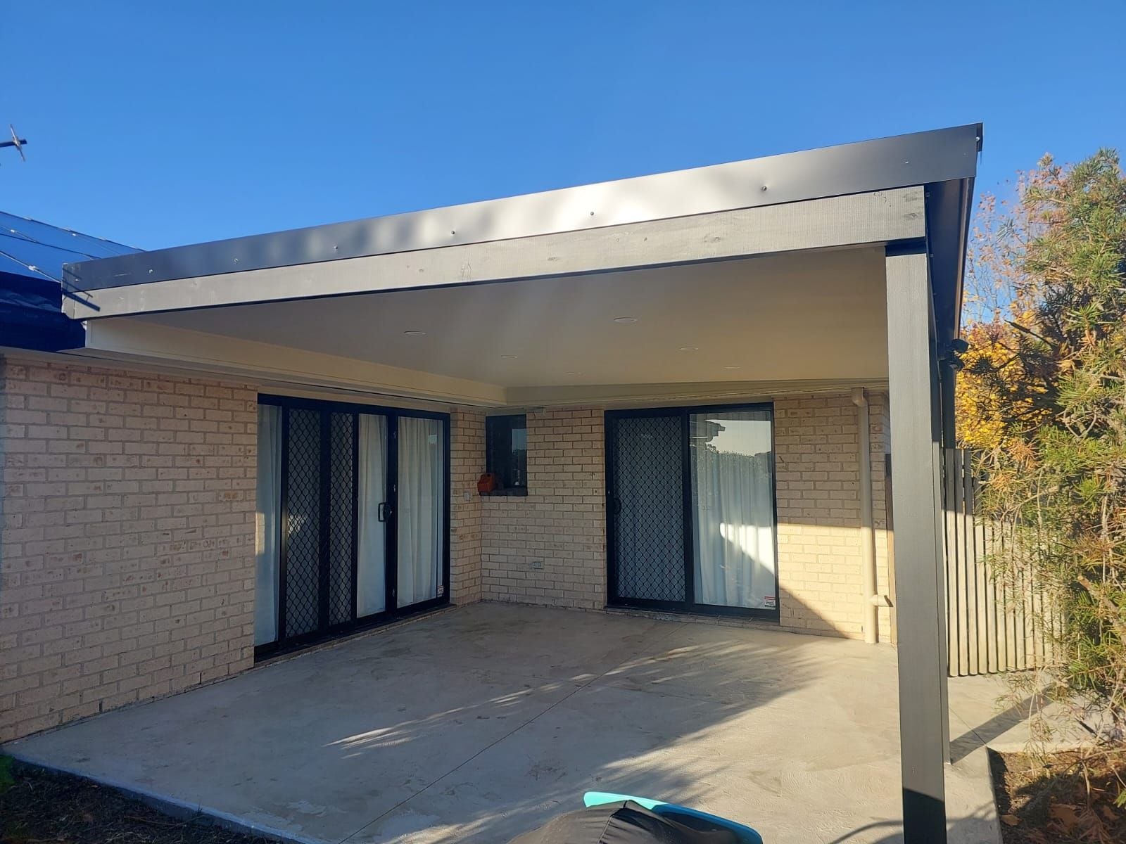 a Covered Patio With Sliding Glass Doors on a Brick House Under a Blue Sky — Elimar Construction in Goulburn, NSW