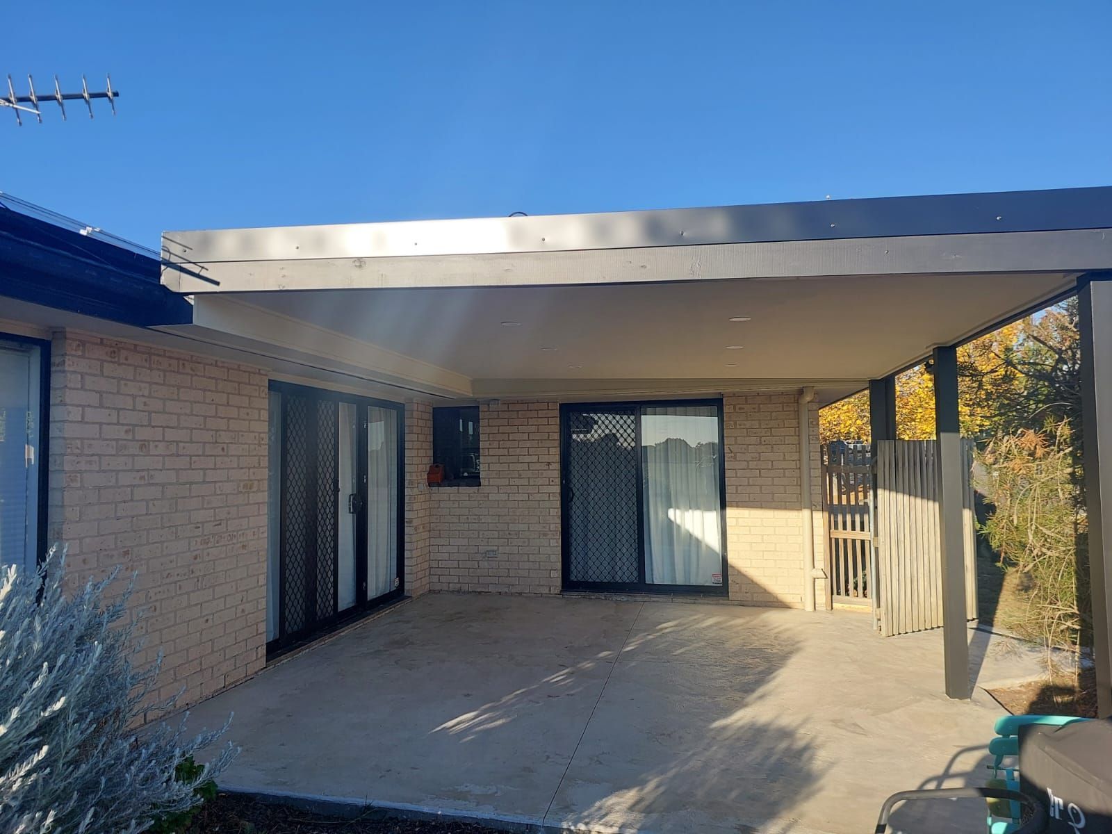 a Patio With Concrete Flooring is Covered by an Attached Roof. the Patio Has Three Sliding Glass Doors  — Elimar Construction in Goulburn, NSW