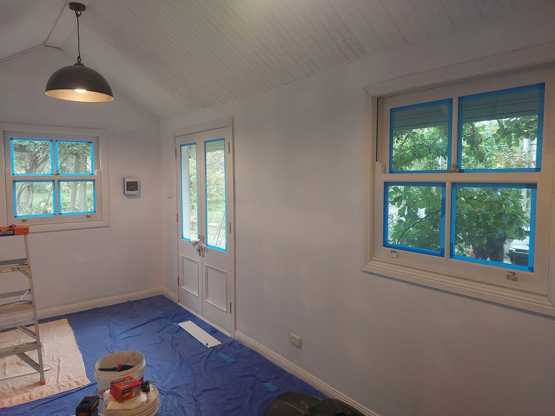 Room With White Walls, a Door, and Two Windows With Blue Tape. a Light Hangs From the Ceiling — Elimar Construction in Goulburn, NSW