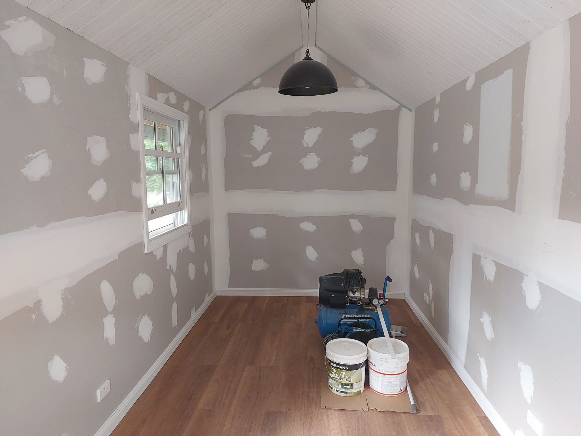 Interior of a Small Room Under Construction With Wood Flooring, Drywall, and a Hanging Light — Elimar Construction in Goulburn, NSW