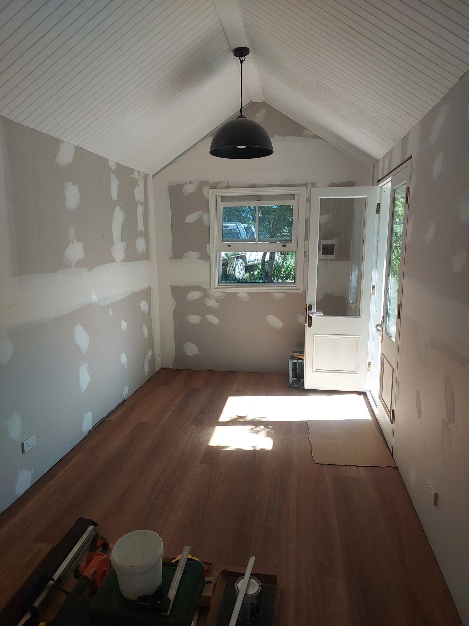 Interior Room With Exposed Wood Floor, Unfinished Walls, and a Hanging Light. Door and Window Provide Natural Light — Elimar Construction in Goulburn, NSW