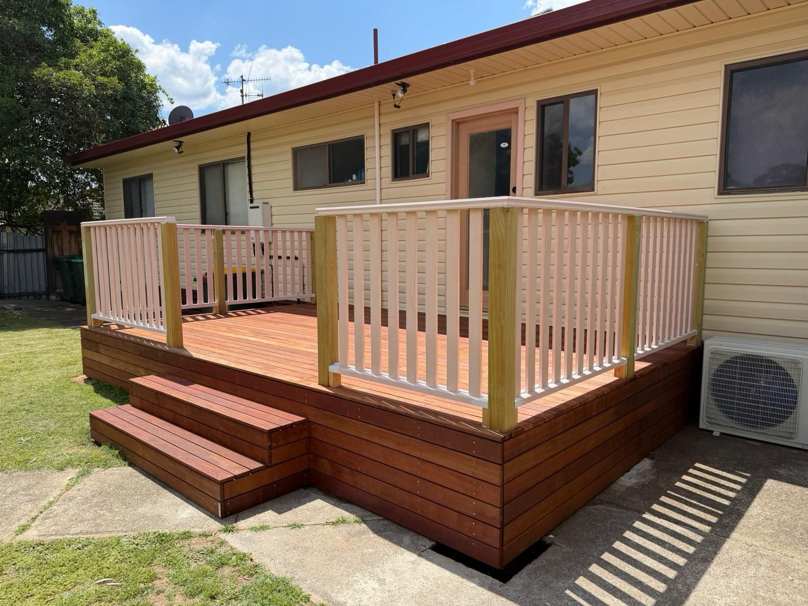 Wooden backyard deck with railing and steps attached to a beige house under sunny skies — Elimar Construction in Goulburn, NSW