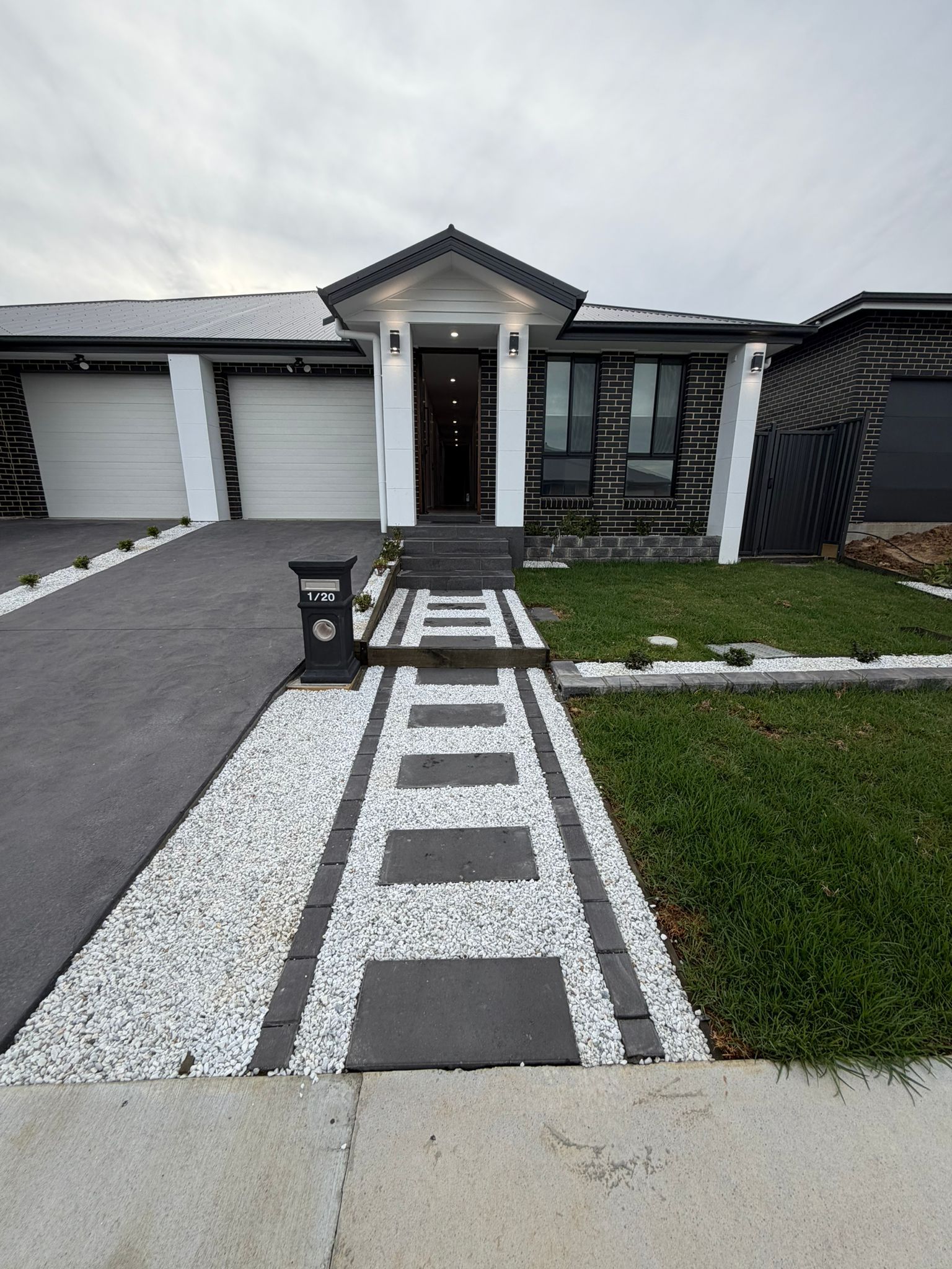 Modern house front entrance with walkway, white garage doors, and gravel landscaping — Elimar Construction in Goulburn, NSW