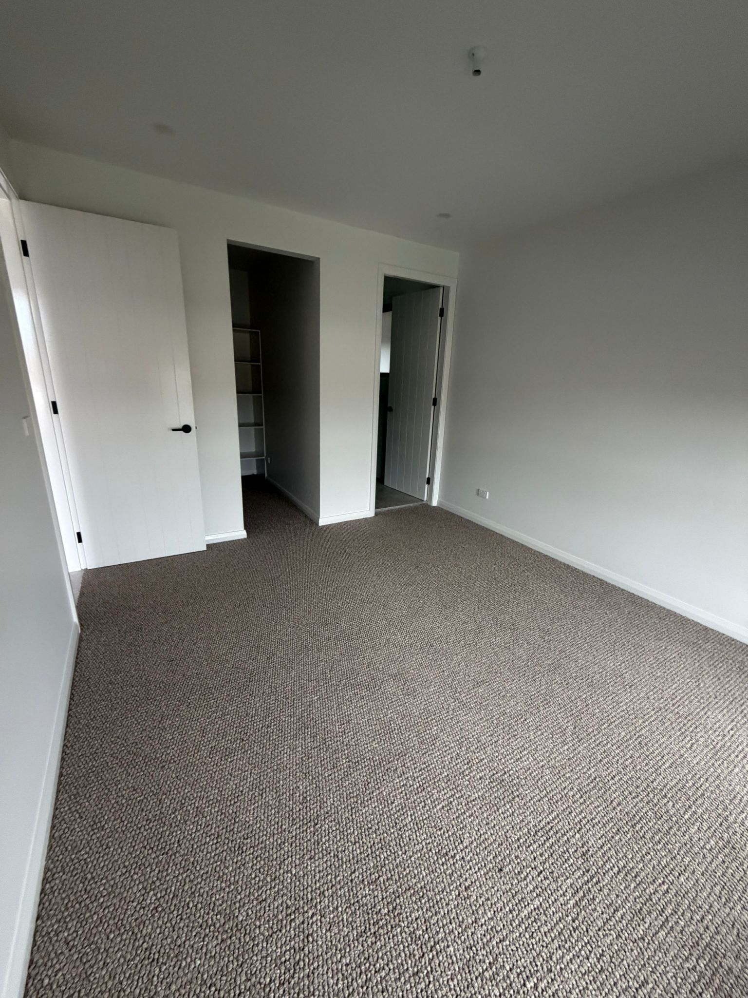 Empty bedroom with patterned carpet, white walls, and open closet and doorway — Elimar Construction in Goulburn, NSW