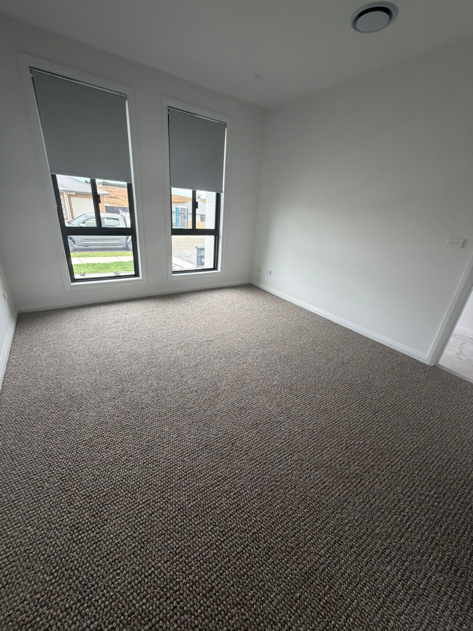 Empty white bedroom with gray carpet and two tall windows — Elimar Construction in Goulburn, NSW