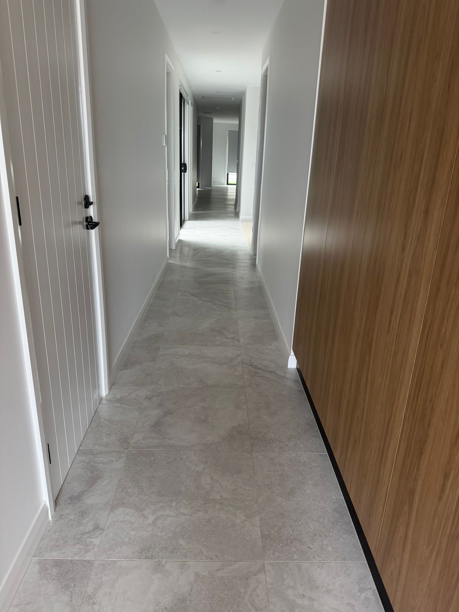 Narrow apartment hallway with white walls, light wood doors, and gray tile floor leading to a distant doorway — Elimar Construction in Goulburn, NSW