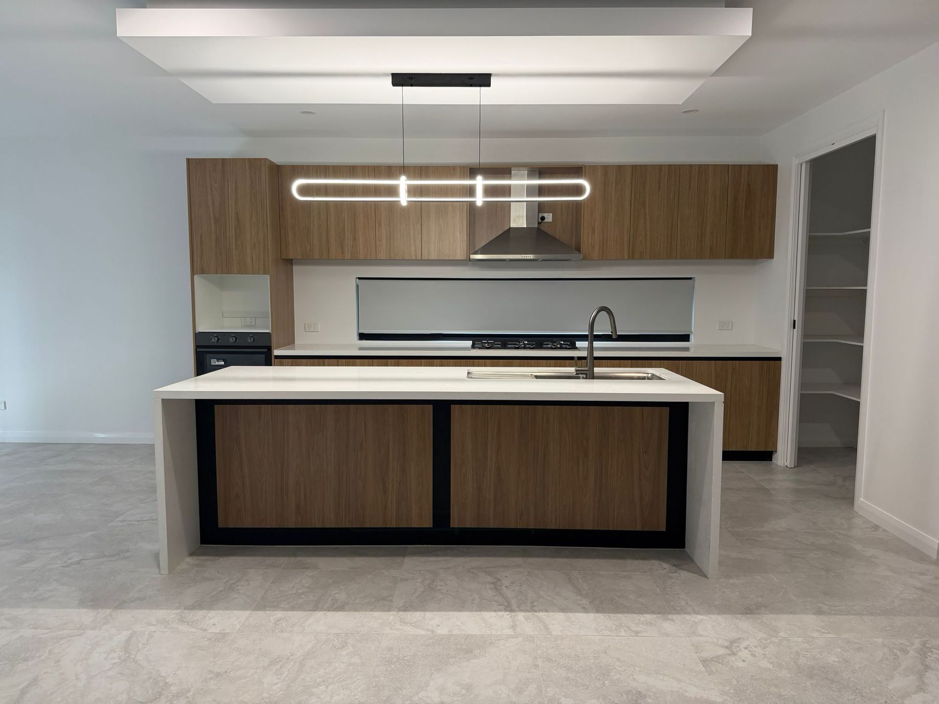 Modern kitchen with wood cabinetry, large island, pendant light, and gray tile floor — Elimar Construction in Goulburn, NSW
