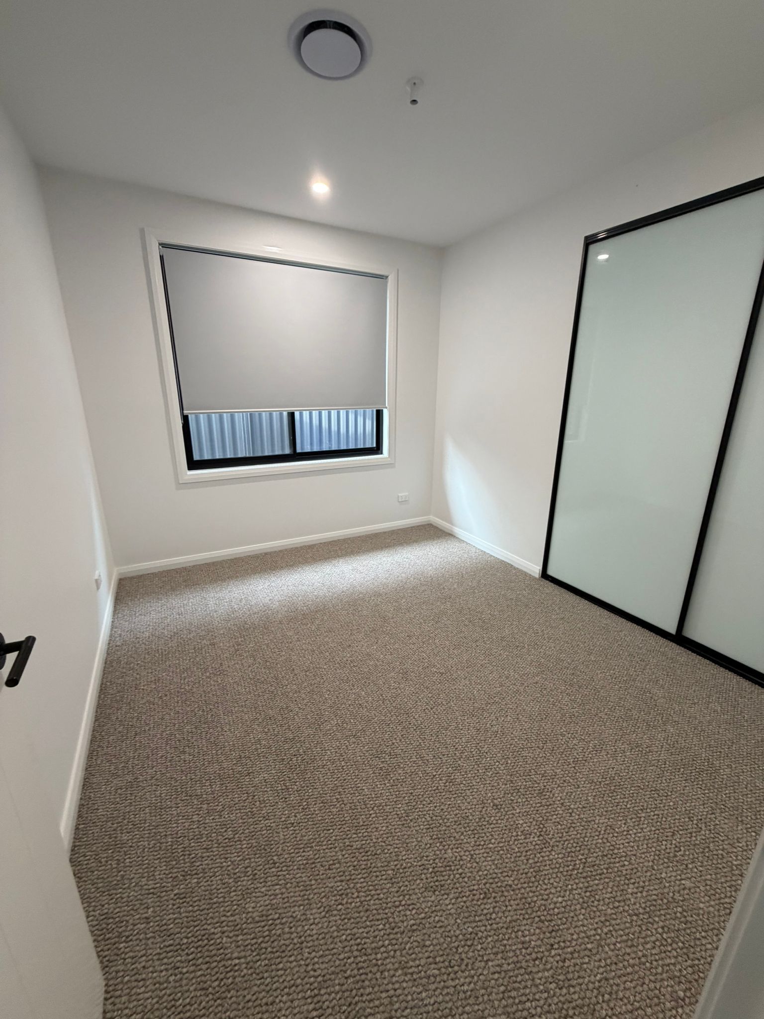 Empty white room with carpeted floor, window blind, ceiling light, and frosted glass door or closet panels — Elimar Construction in Goulburn, NSW