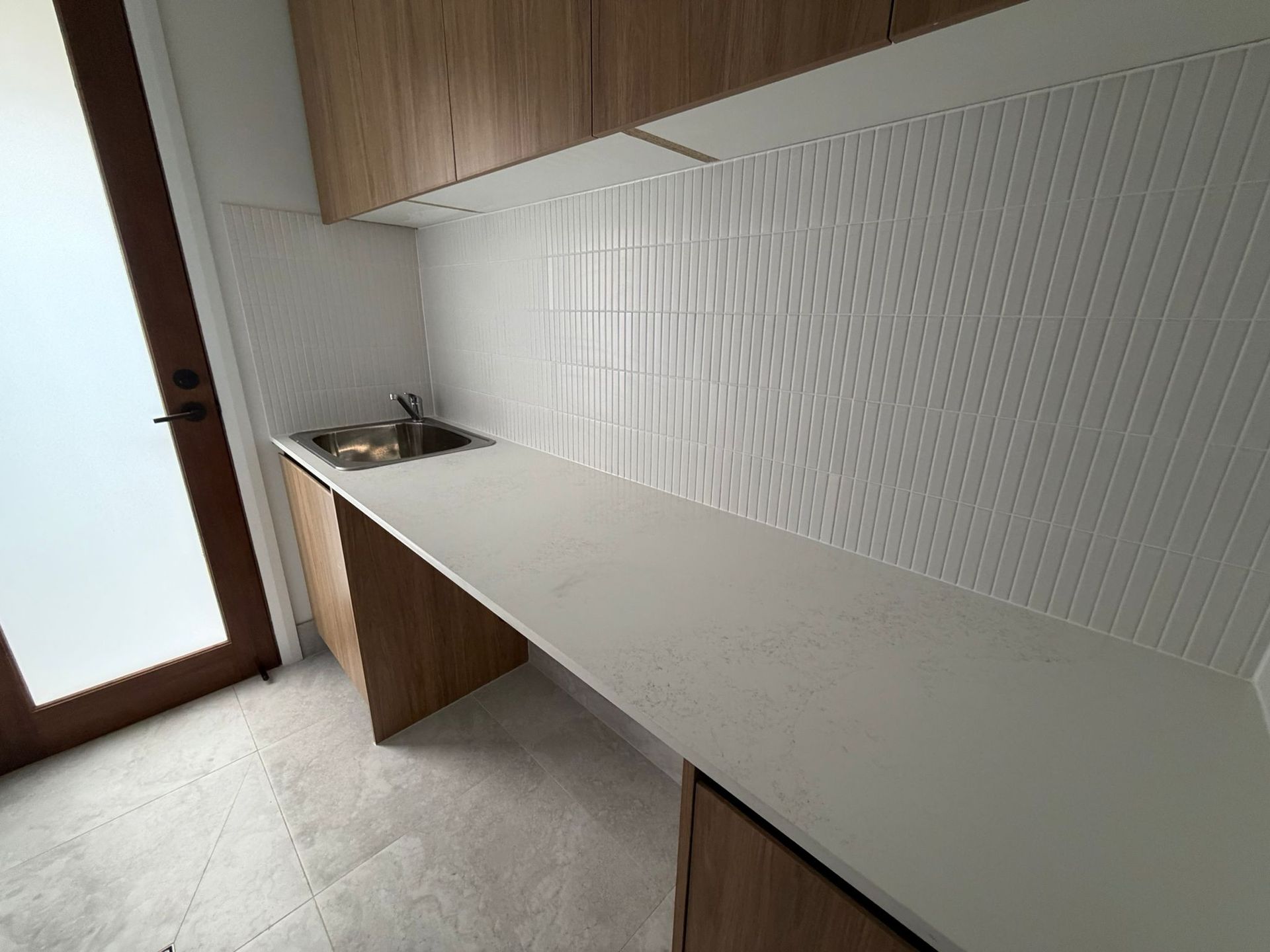 Modern kitchen counter with white textured backsplash and wooden cabinets near a door — Elimar Construction in Goulburn, NSW