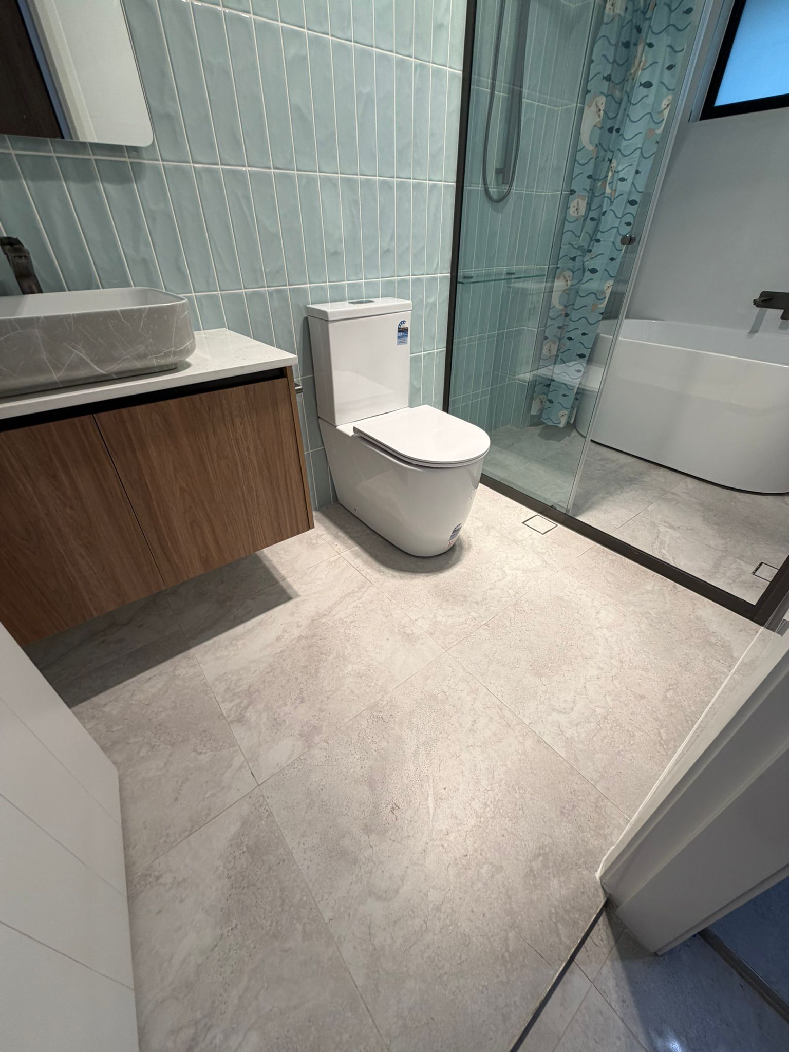 Modern bathroom with toilet, vanity, glass shower, and light gray tile flooring — Elimar Construction in Goulburn, NSW