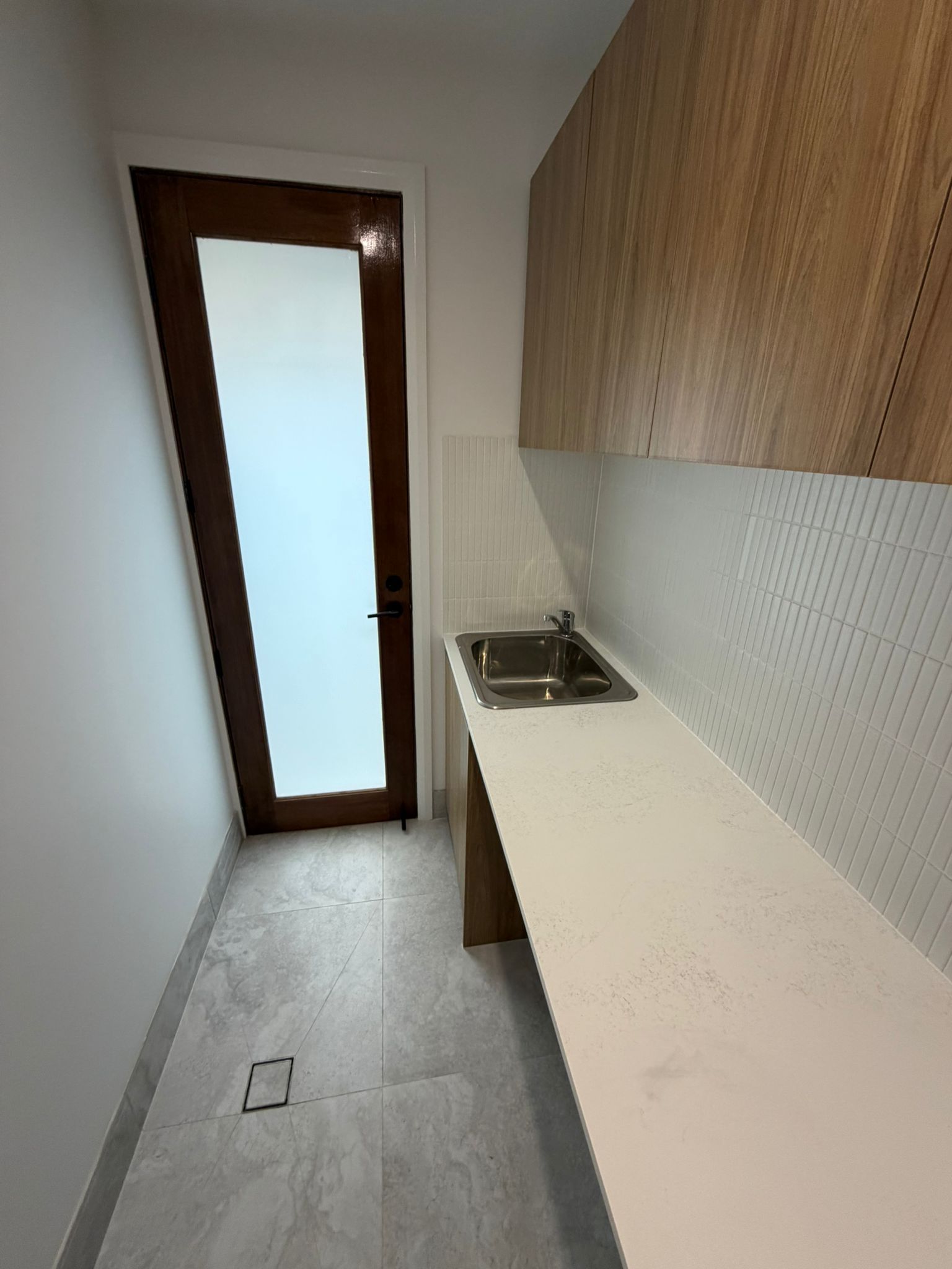 Narrow modern kitchen with white countertops, wood cabinets, sink, and frosted glass door — Elimar Construction in Goulburn, NSW
