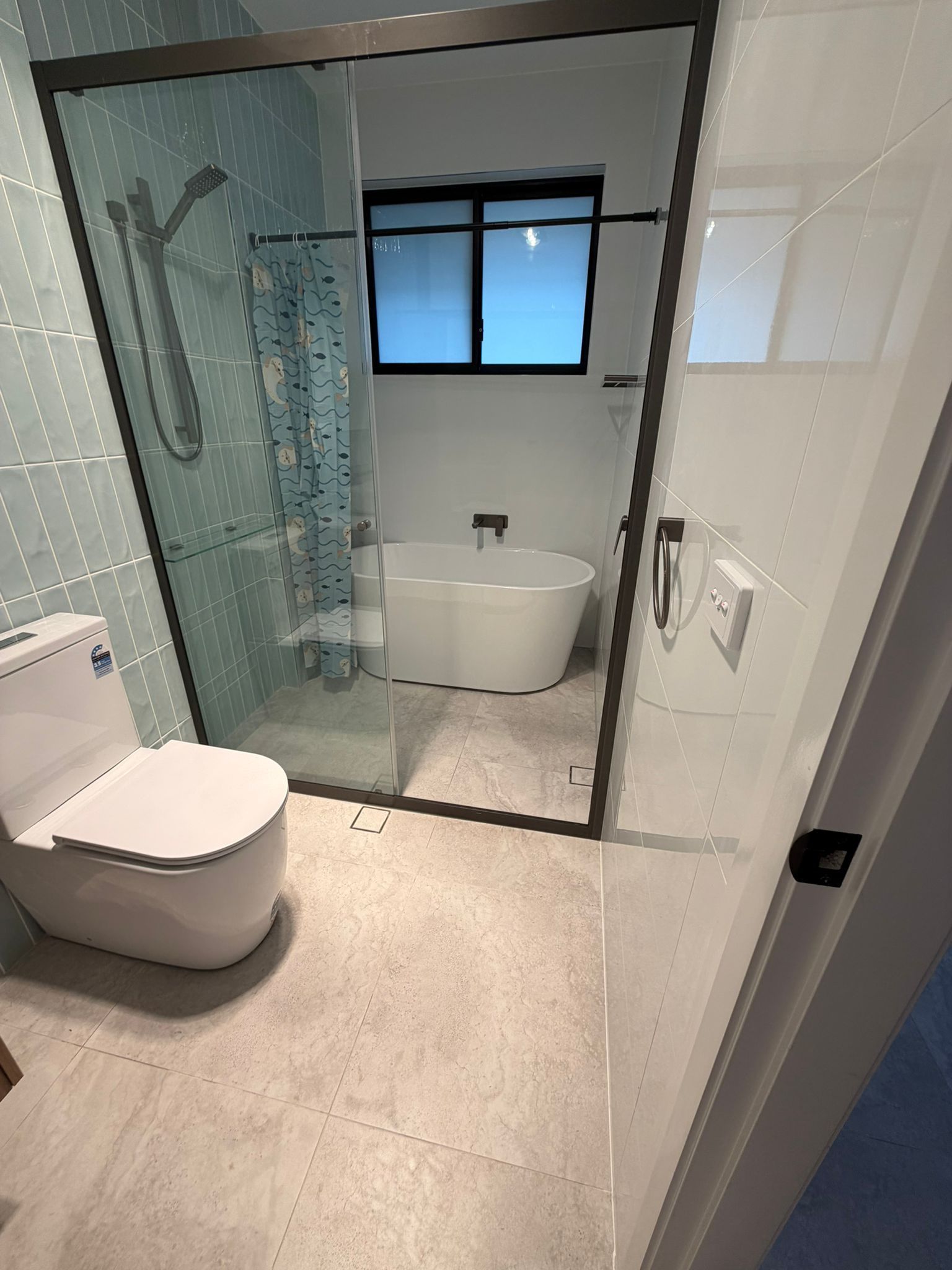 Modern bathroom with toilet, glass shower, freestanding tub, and tiled walls — Elimar Construction in Goulburn, NSW