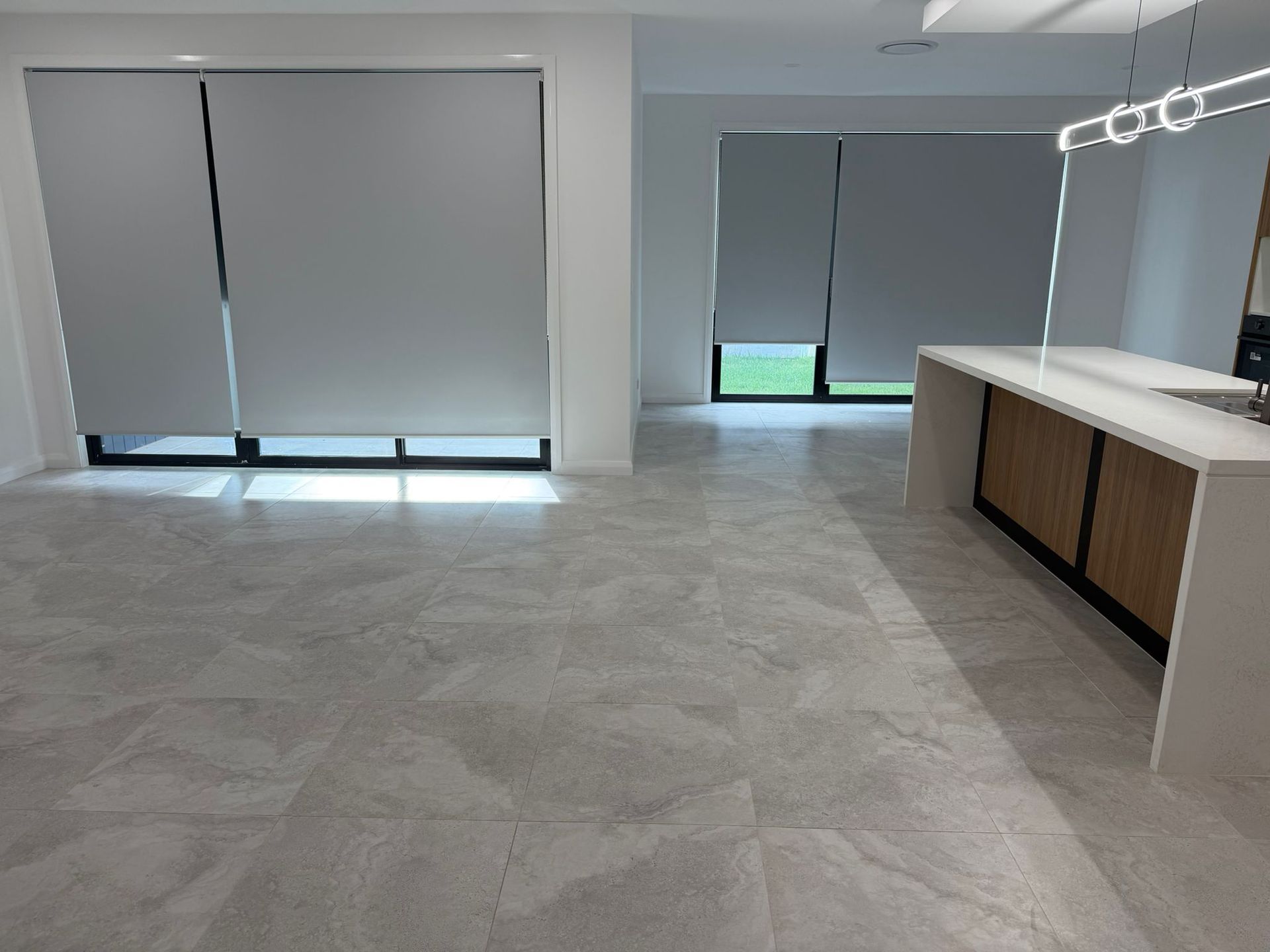Empty modern room with gray tiled floor, closed blinds, and a bathroom vanity on the right — Elimar Construction in Goulburn, NSW