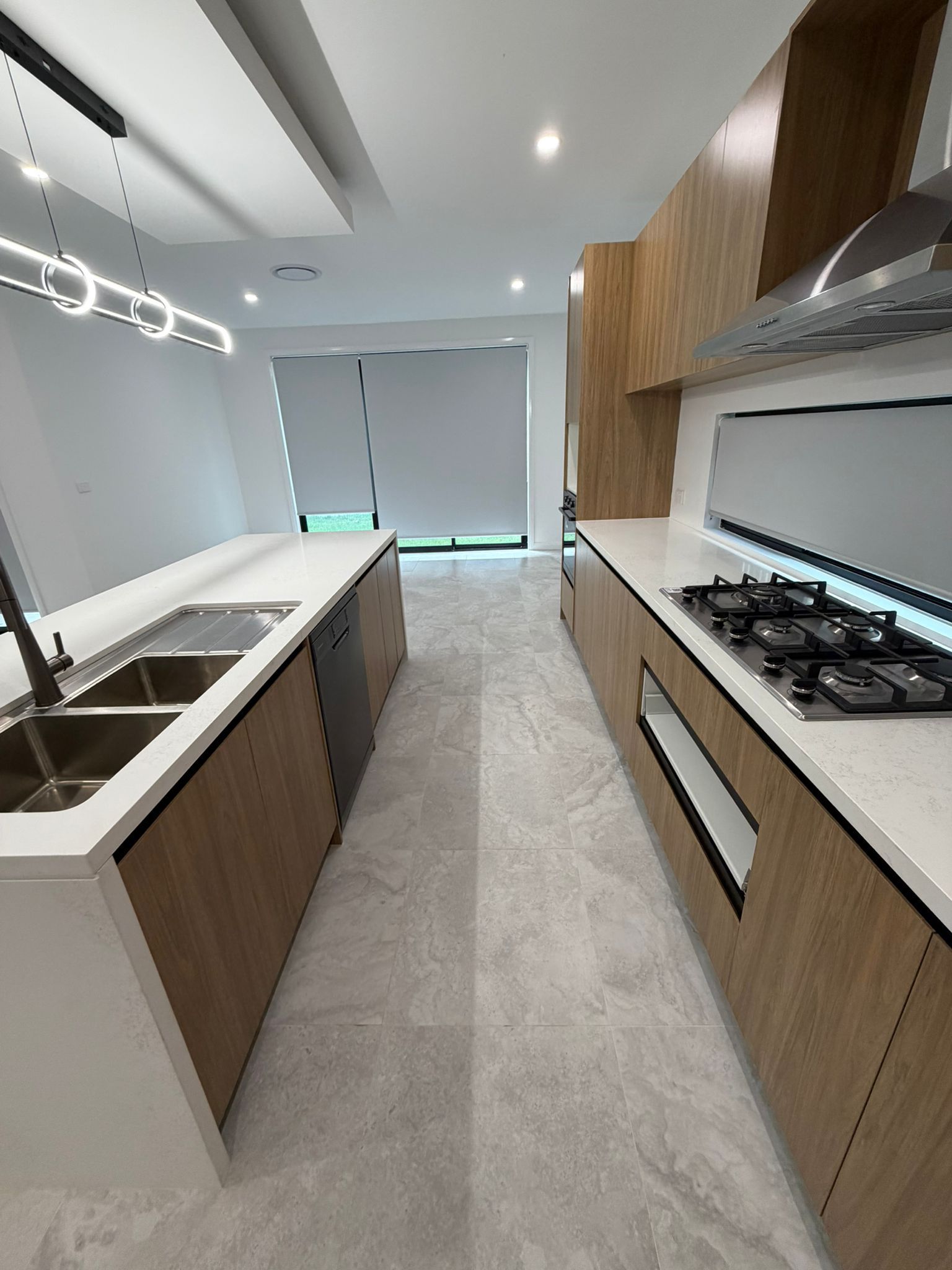 Modern galley kitchen with wood cabinets, white countertops, gas stove, sink, and gray tile floor — Elimar Construction in Goulburn, NSW