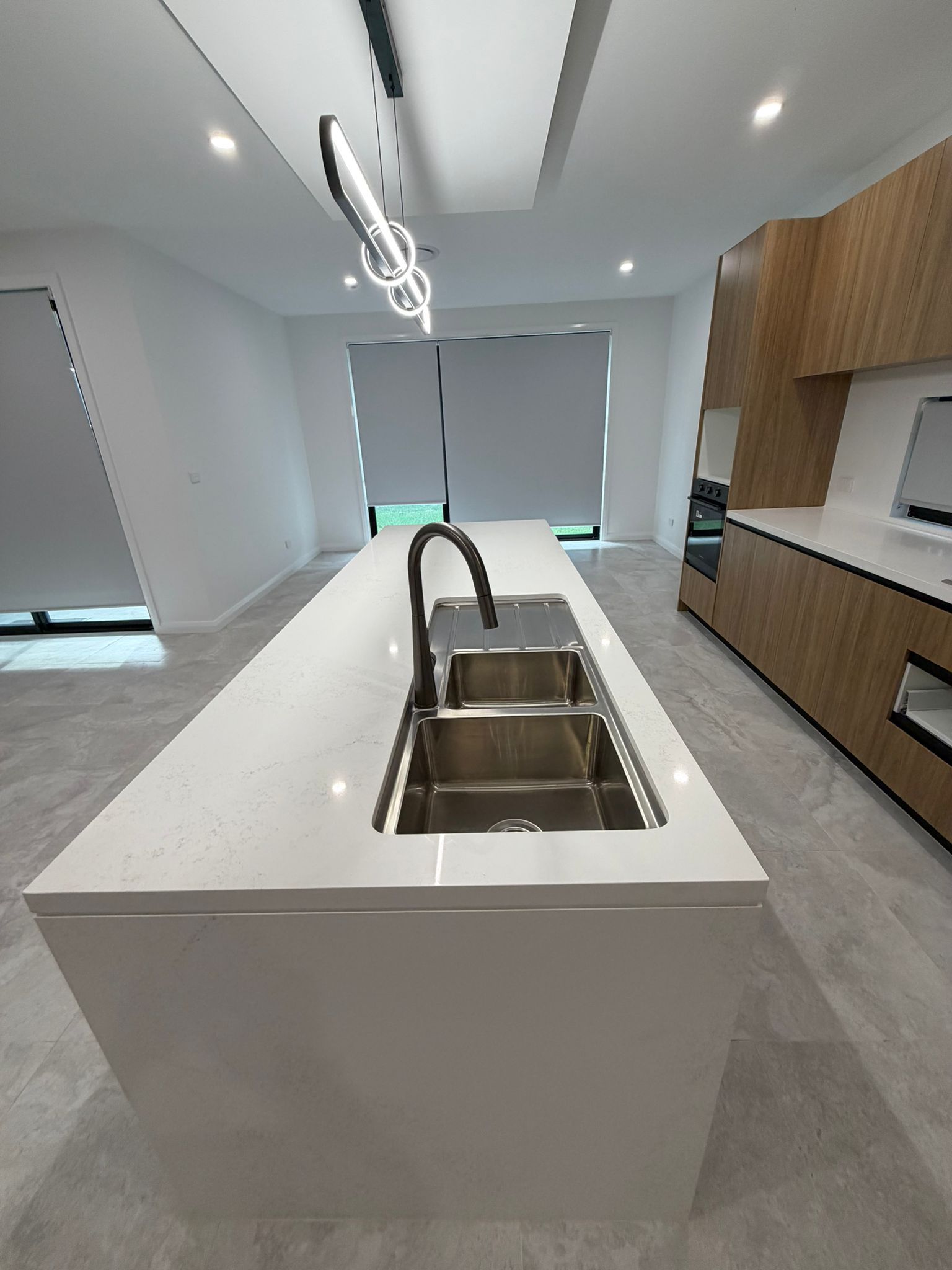 Modern kitchen with white island, stainless steel sink, wood cabinets, and large windows — Elimar Construction in Goulburn, NSW