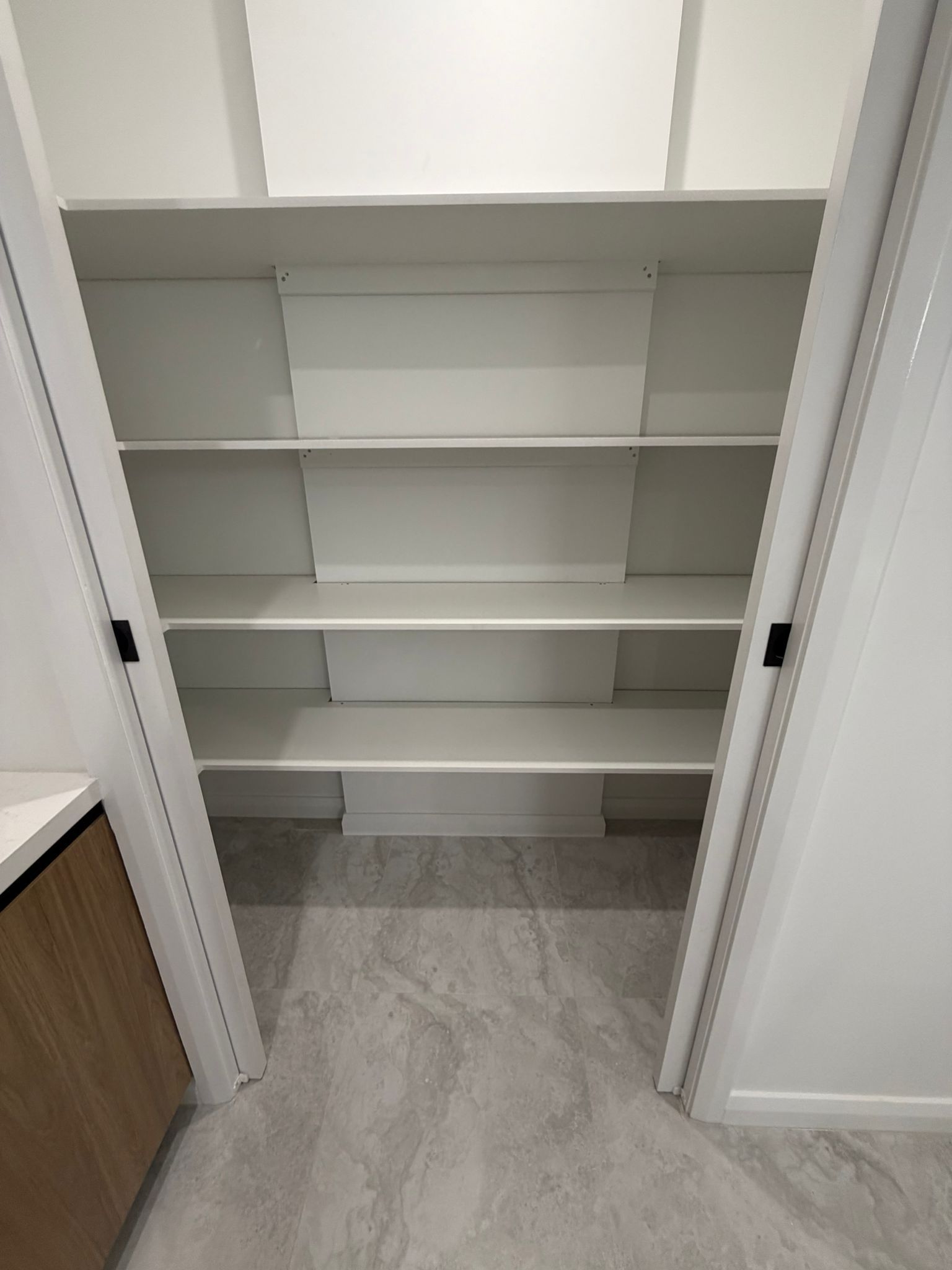 Empty white closet with built-in shelves and gray flooring — Elimar Construction in Goulburn, NSW