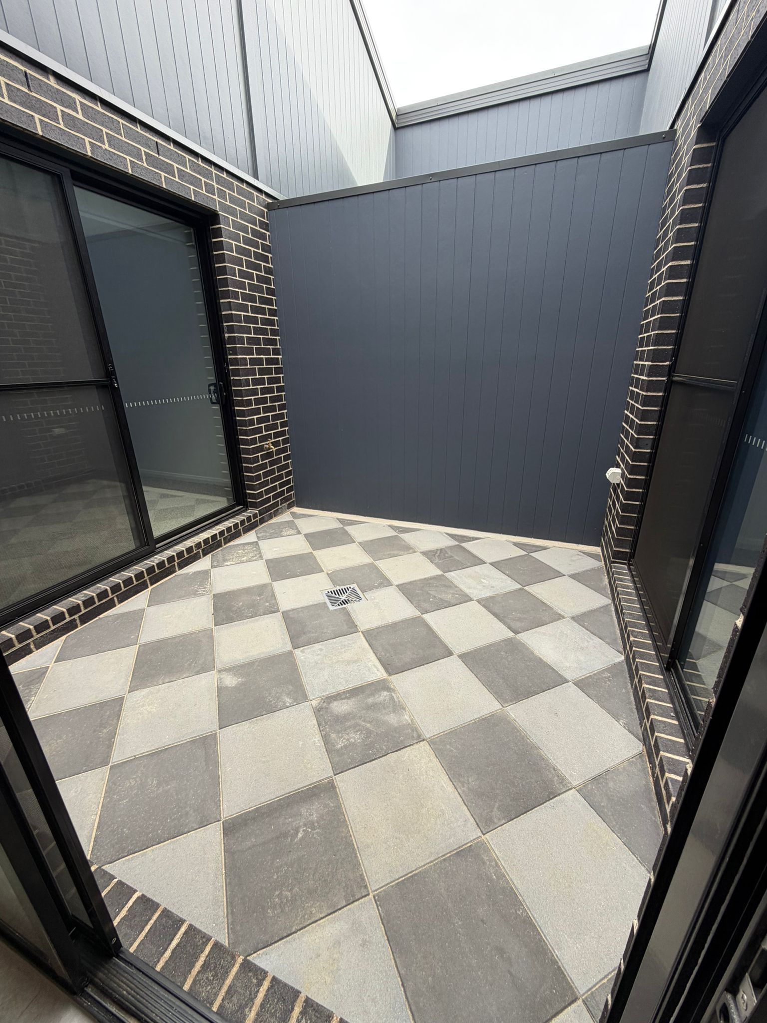 Small tiled patio with gray walls, checkered floor, and large dark windows on the left — Elimar Construction in Goulburn, NSW
