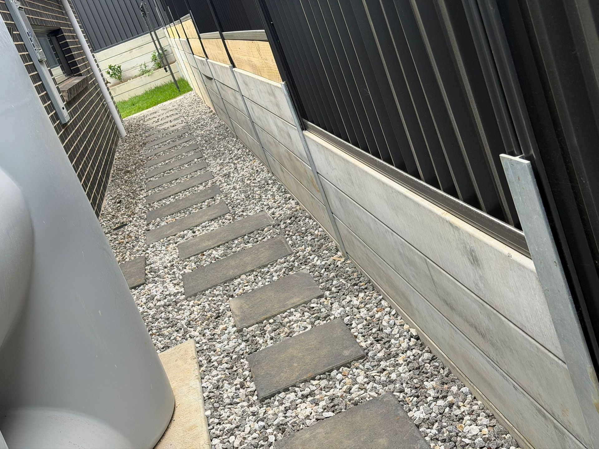 Narrow gravel walkway with stepping stones between black fence and concrete wall — Elimar Construction in Goulburn, NSW