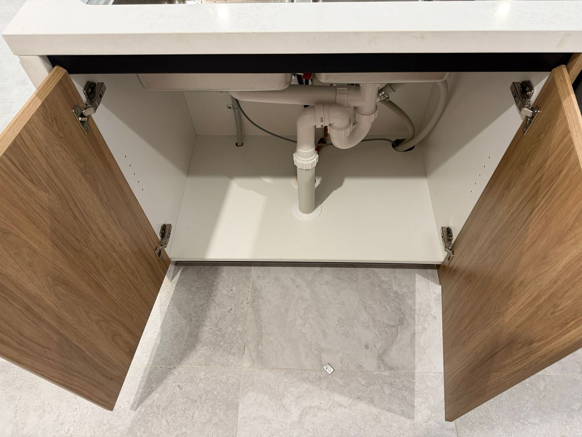 Open bathroom vanity cabinet with sink plumbing and two wooden doors — Elimar Construction in Goulburn, NSW