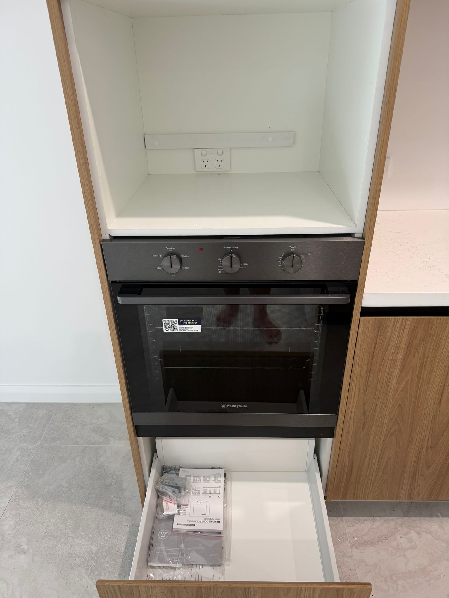Built-in oven and empty cabinet shelf with white walls and wood trim inside a kitchen unit — Elimar Construction in Goulburn, NSW