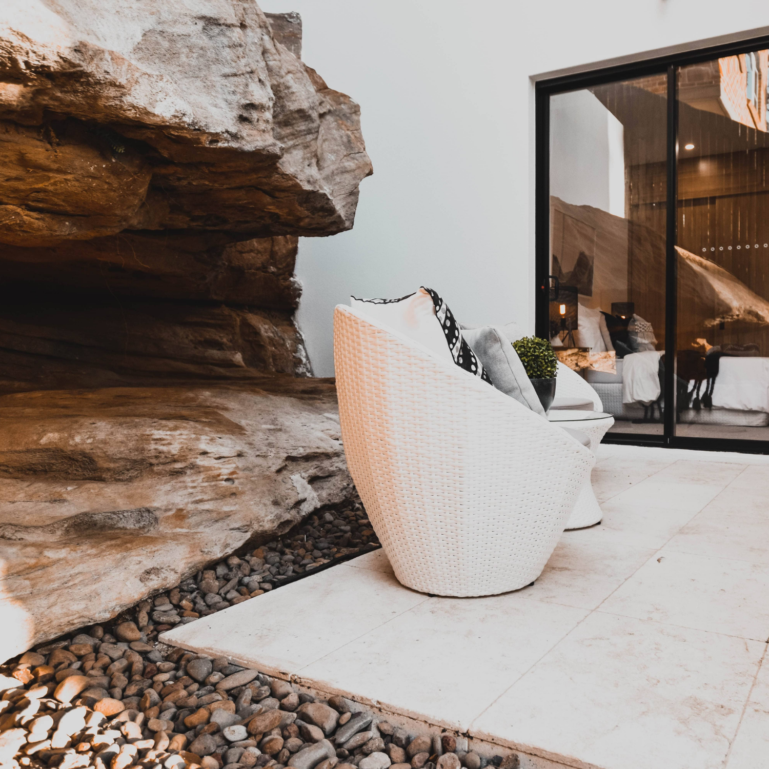 White Wicker Chair Next to Large Rock Formation and Glass Door — Elimar Construction in Yass, NSW