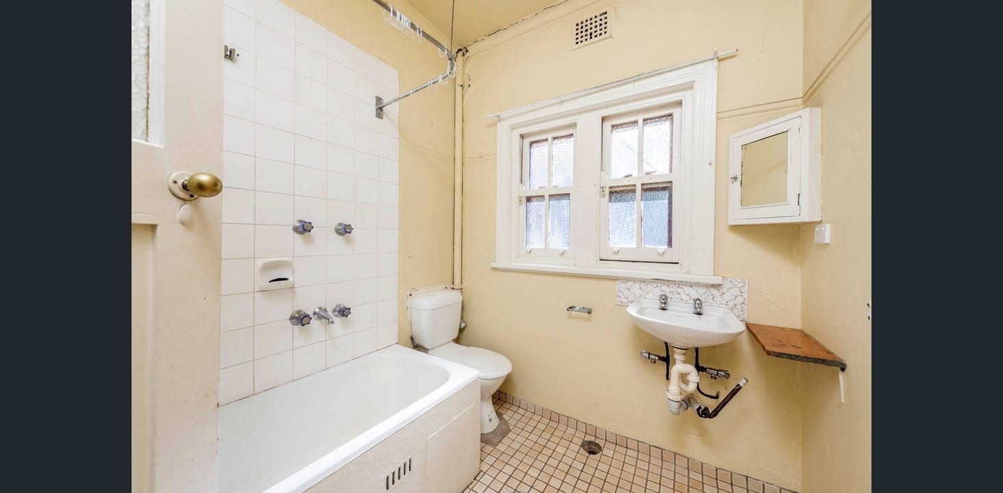 Small, Yellow-walled Bathroom With a White Bathtub, Toilet, and Sink. Windows and a Small Cabinet on the Wall  — Elimar Construction in Goulburn, NSW