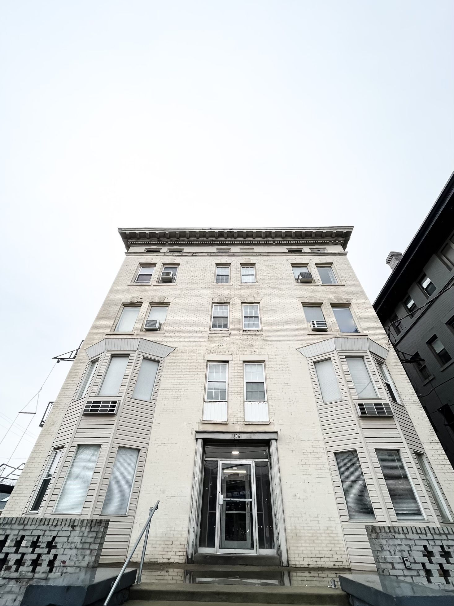 Five-story white brick building with dark doorway and air conditioning units on each floor.
