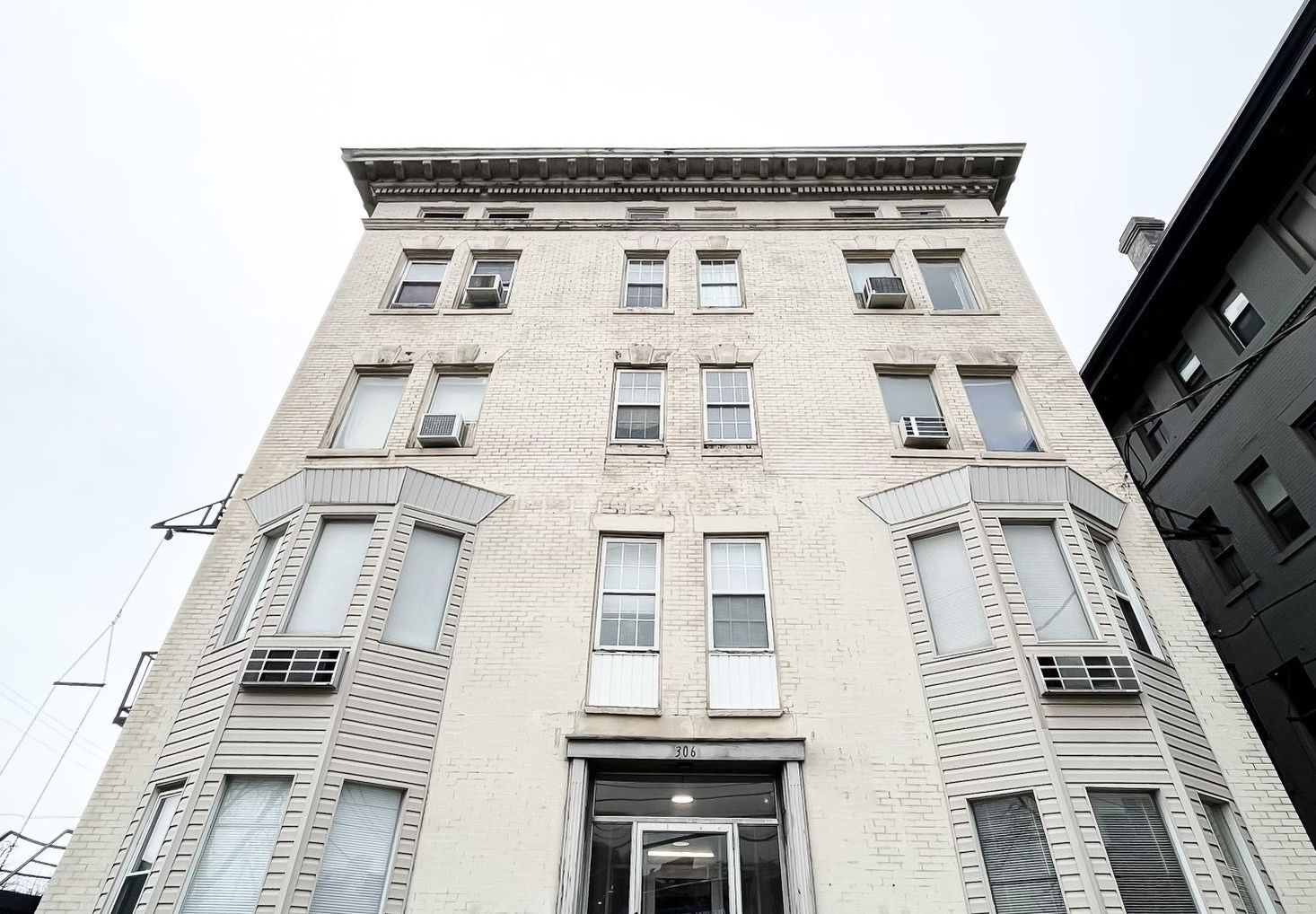 A tall, light brick building with several windows and a dark entryway, shot from a low angle.