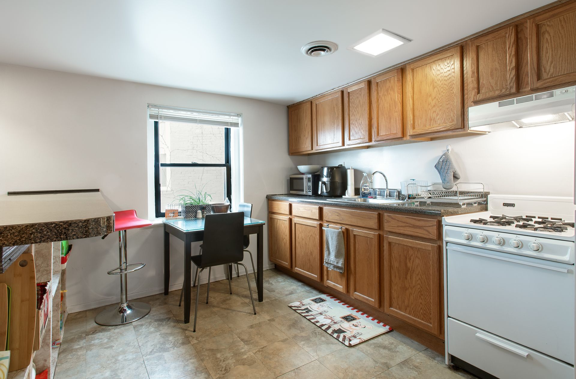 Kitchen with wooden cabinets, small table, window, and white appliances.