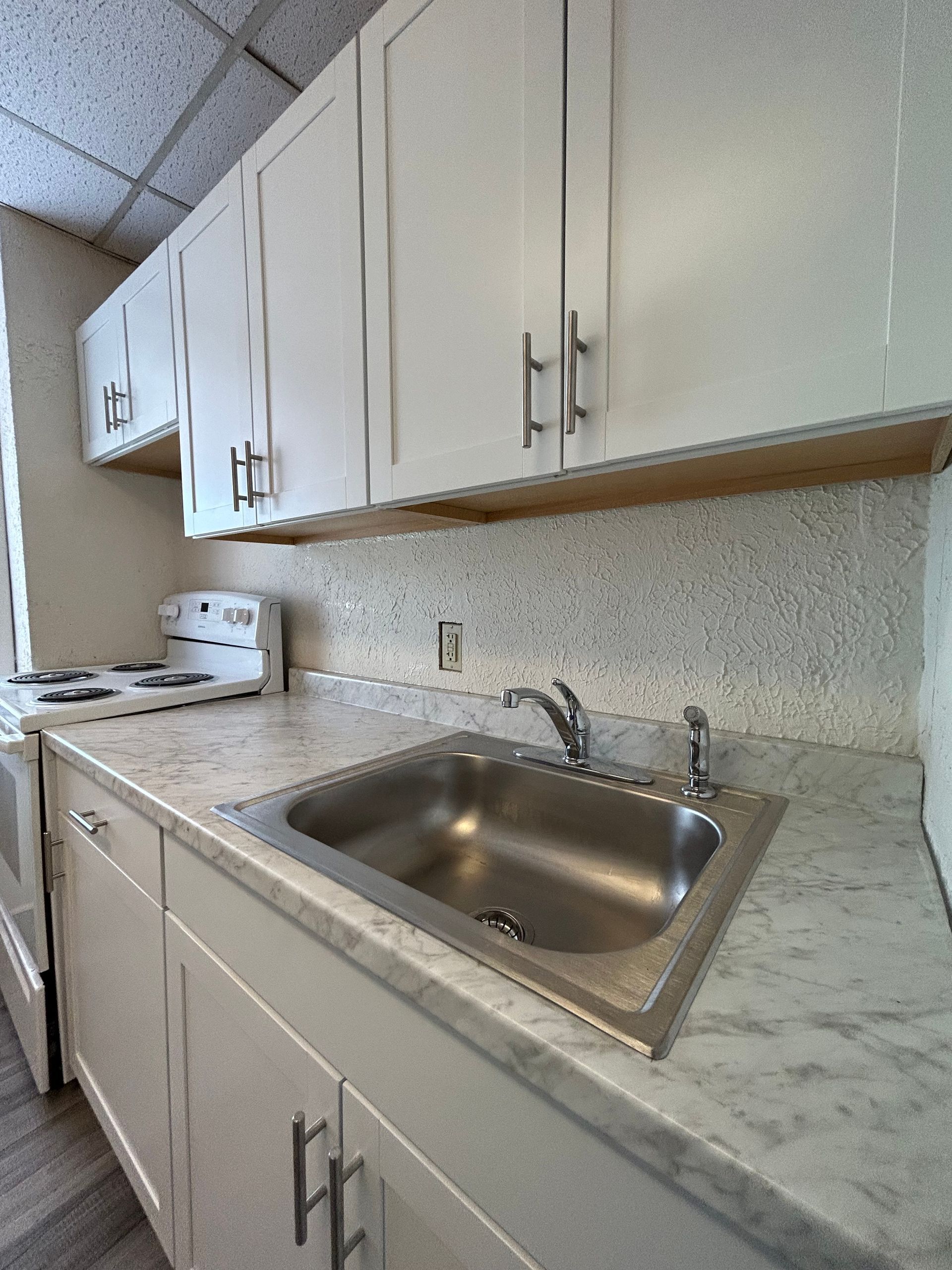 Small kitchen with white cabinets, a stainless steel sink, and a white stovetop.