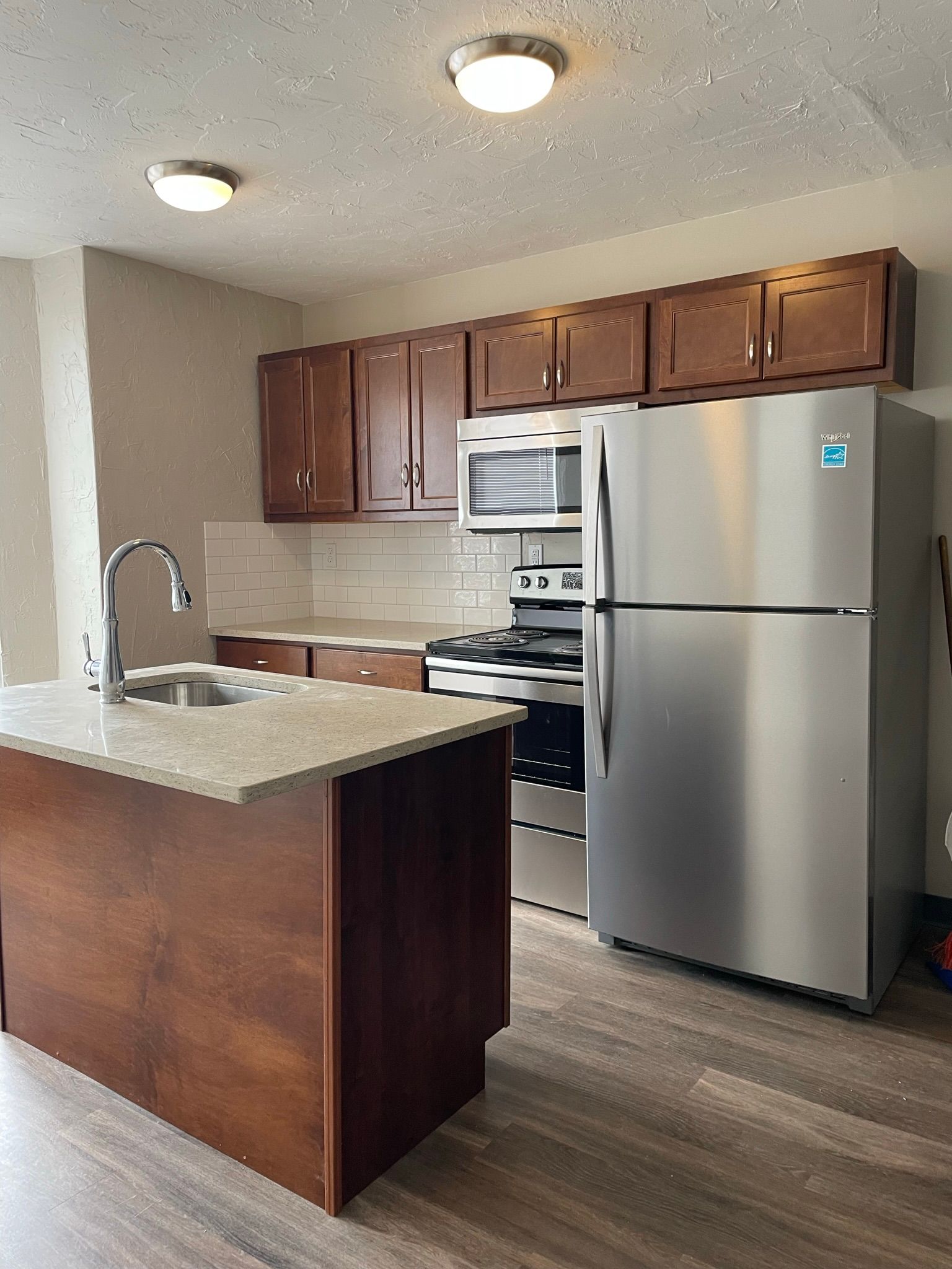 Kitchen with dark cabinets, stainless steel appliances, light-colored countertops, and a kitchen island.