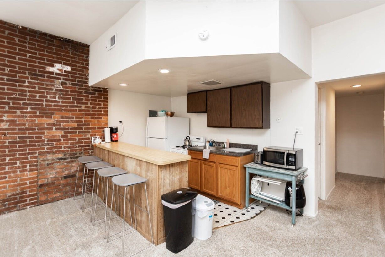 Kitchen with brick wall, wooden bar, stools, and microwave on a cart.