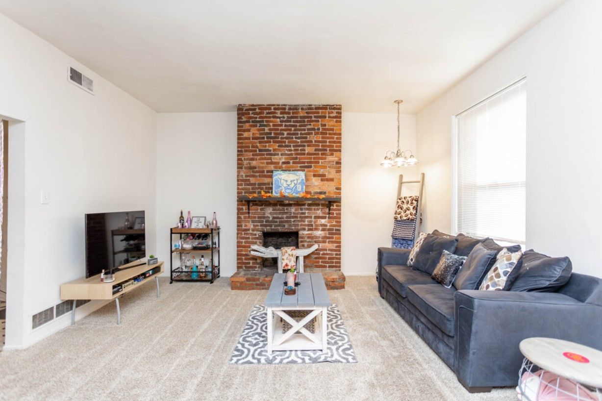 Living room with brick fireplace, blue couch, and light-colored carpet.