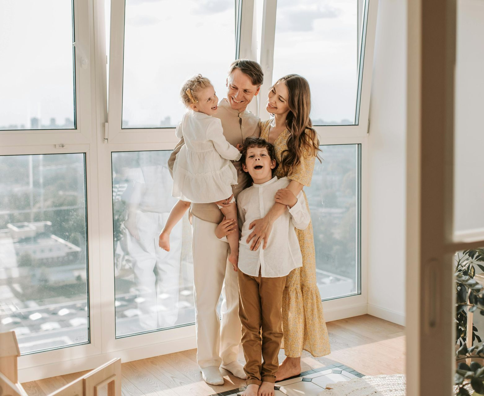 Family of four smiling together near a large window.