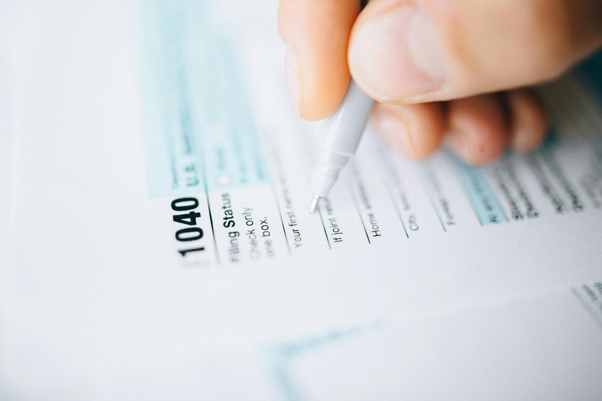 Hand writing on a 1040 tax form with a pen, filling out paperwork.