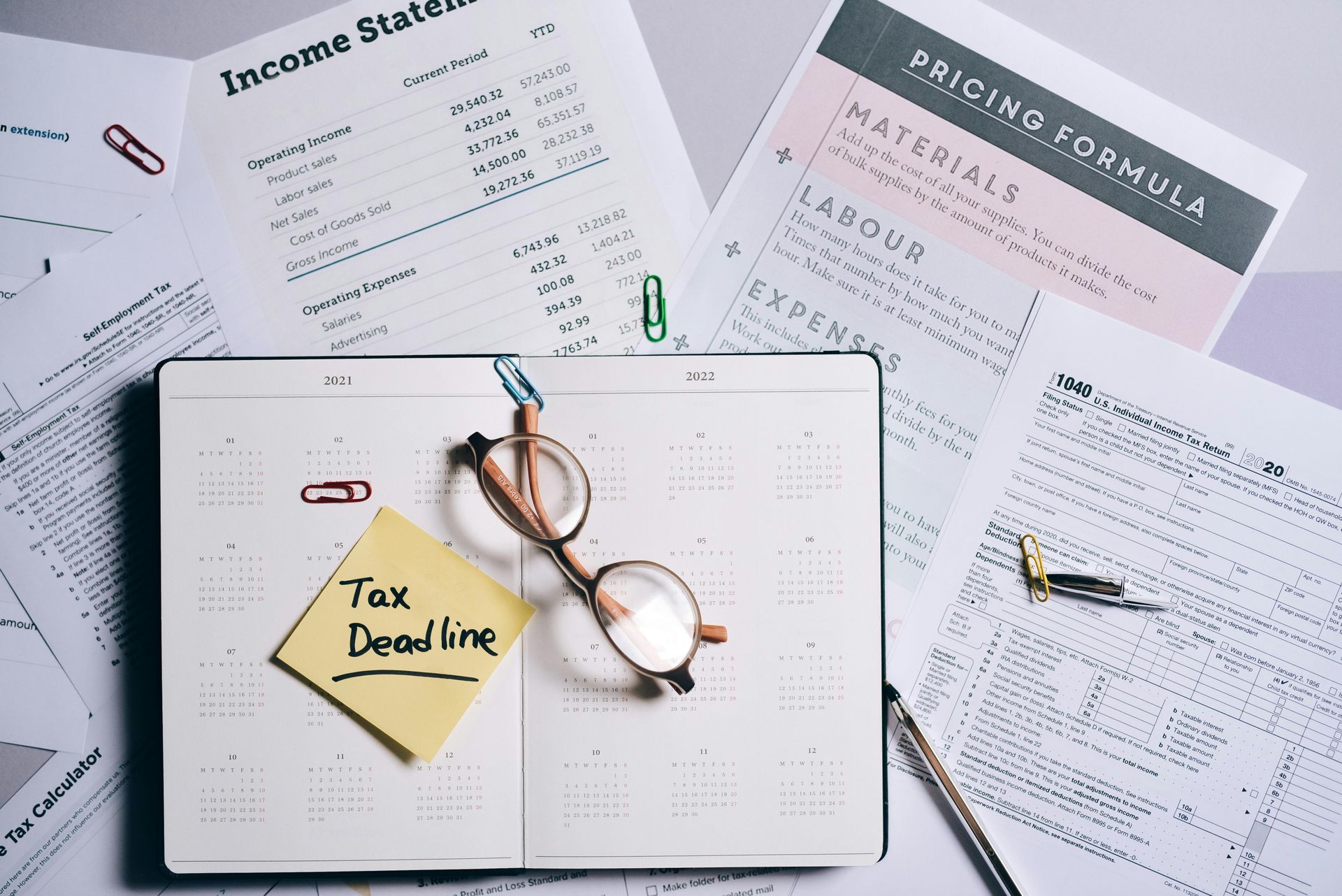 Desk with tax documents, glasses, calendar, and a sticky note that reads, 