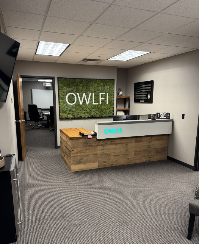 Reception area of OWLFI with a wooden reception desk and a green wall with the logo.