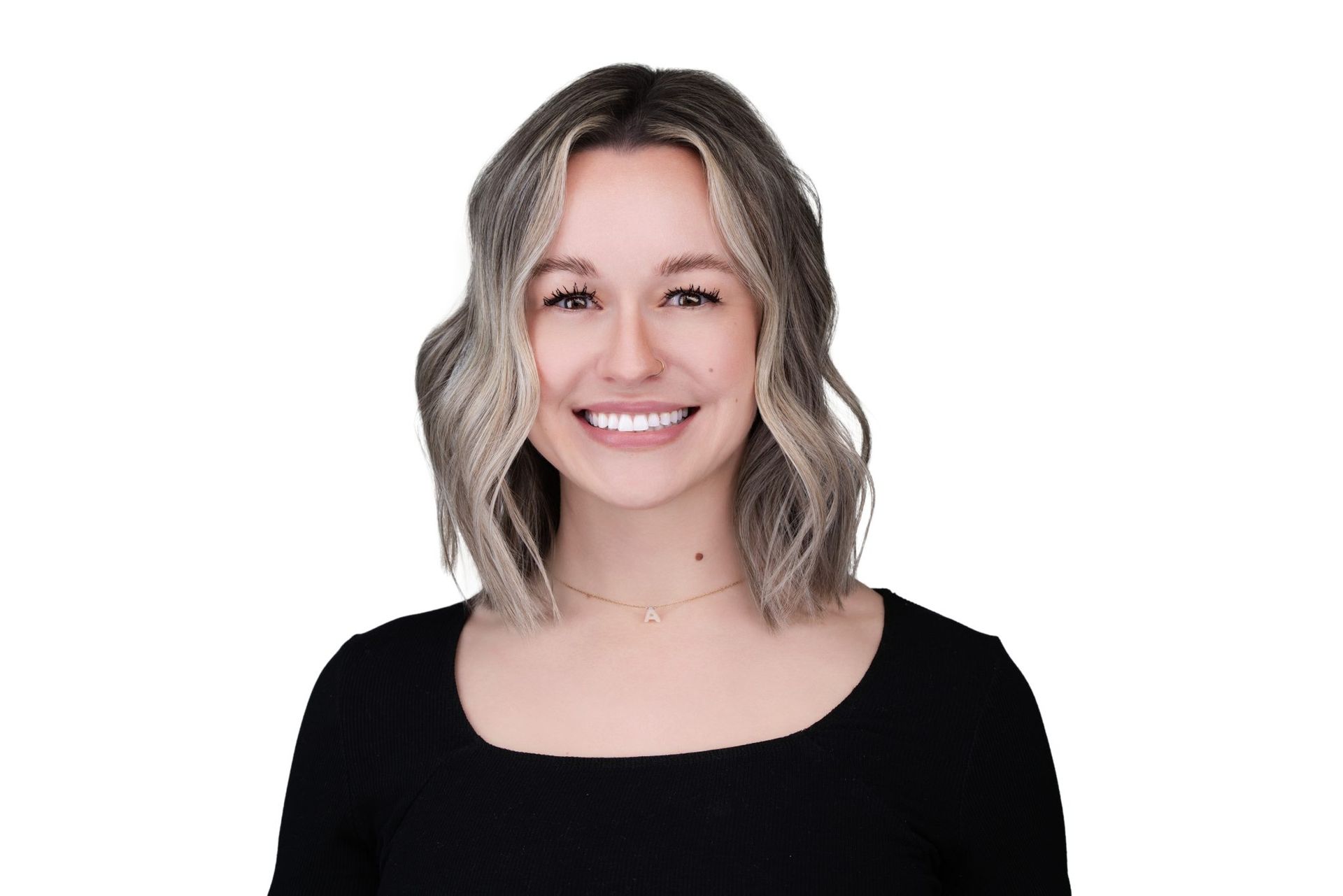 Woman with blonde wavy hair, smiling, wearing a black top and gold necklace.
