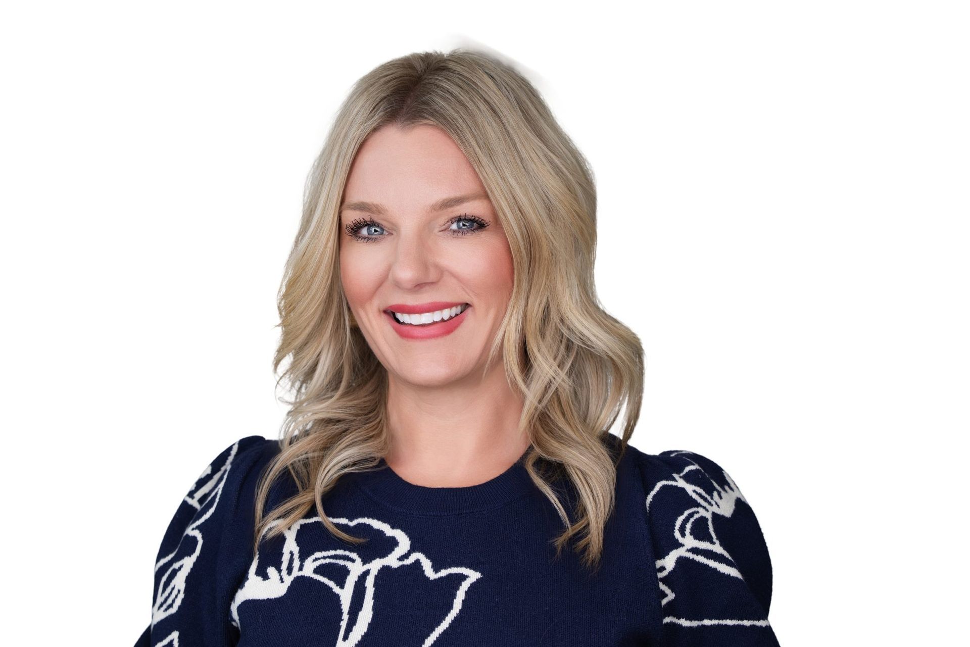 Woman with blonde hair smiling, wearing a navy blue top with white floral design.