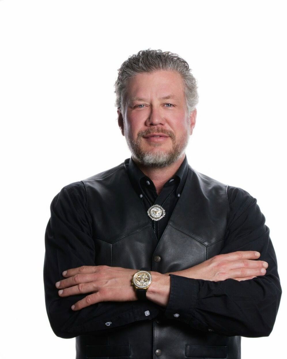 Man in black leather vest, arms crossed, smiling.