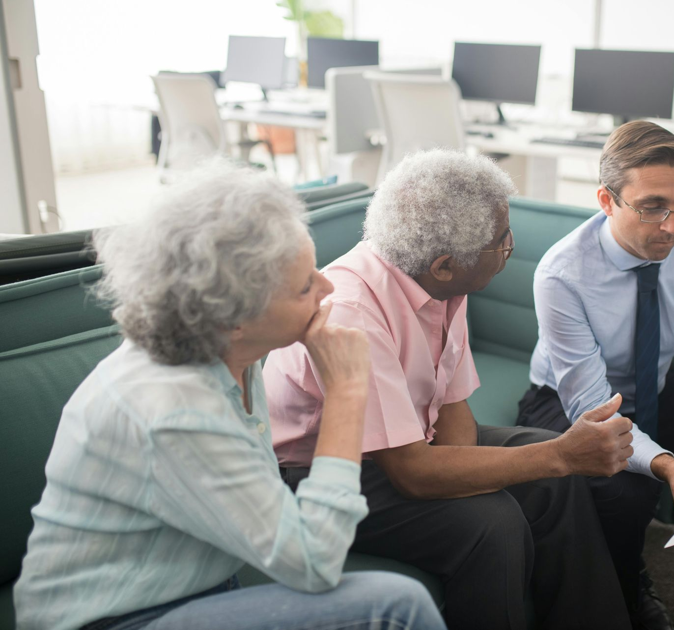 Three people, two older adults and a man, sit on a couch in an office, possibly discussing paperwork.