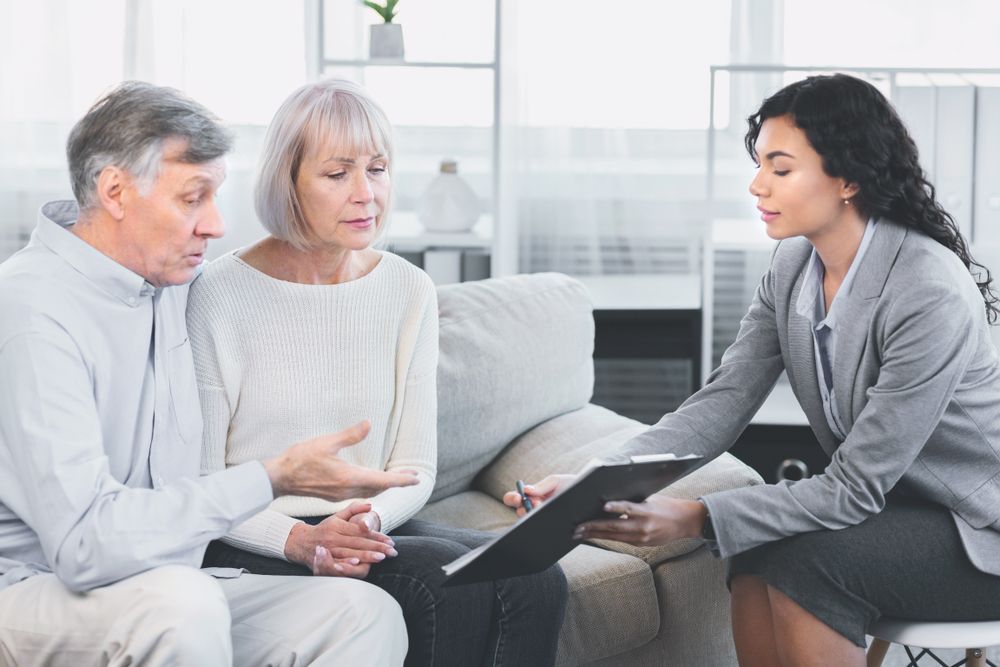 Woman in blazer reviews paperwork with older couple on a couch.