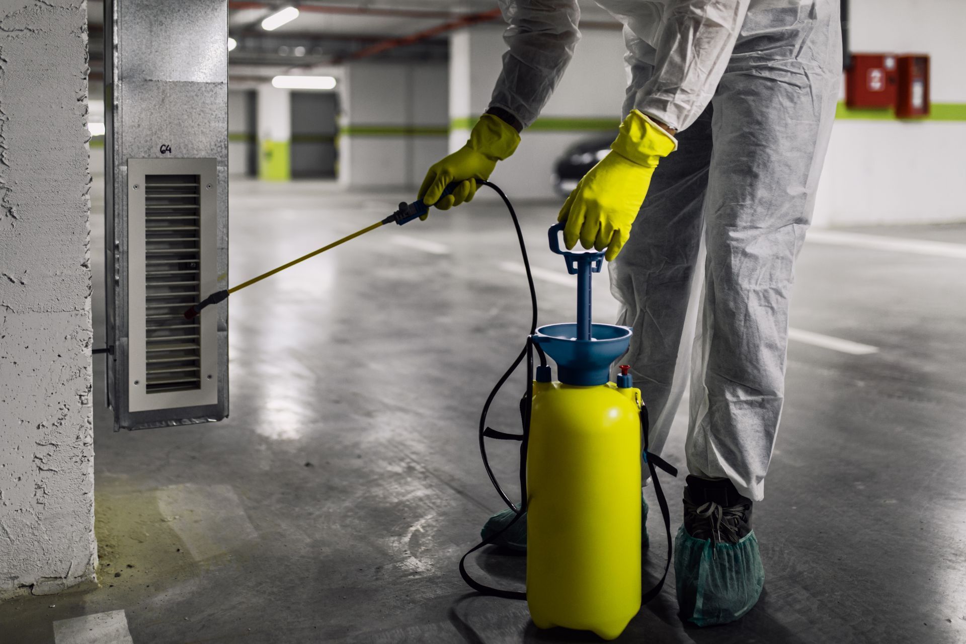 A man in a protective suit is spraying a drain in a parking garage.