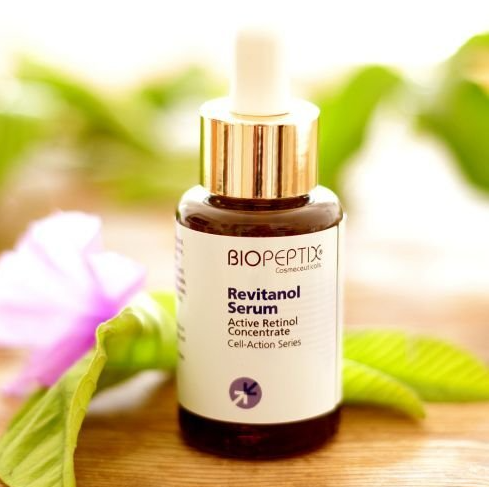 A bottle of biopeptix revitanol serum is sitting on a wooden table.