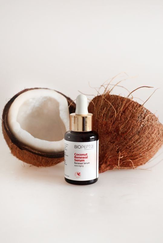 A bottle of serum is sitting next to a coconut.