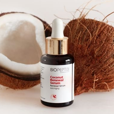 A bottle of biopeptide coconut renewal serum next to a coconut