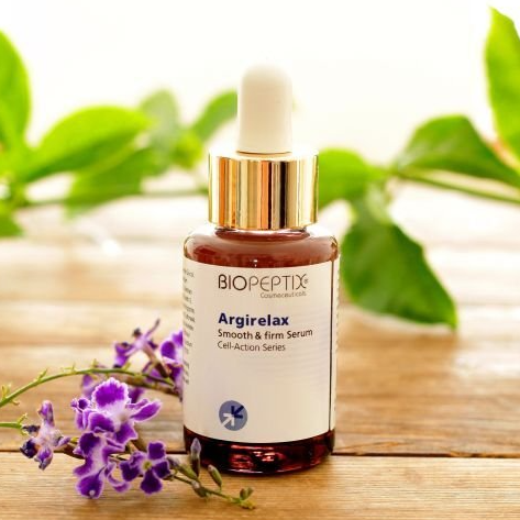 A bottle of biopeptix argirelax is sitting on a wooden table next to purple flowers.