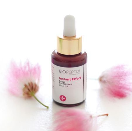 A bottle of biopeptide instant effect next to pink flowers