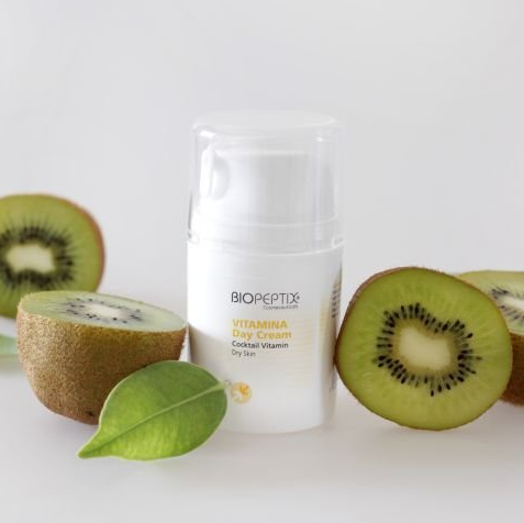 A bottle of biopeptide vitamina day cream next to kiwi slices