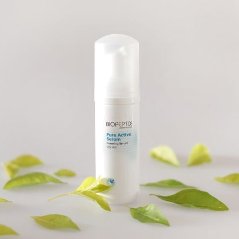 A bottle of biopeptide pure active serum surrounded by green leaves